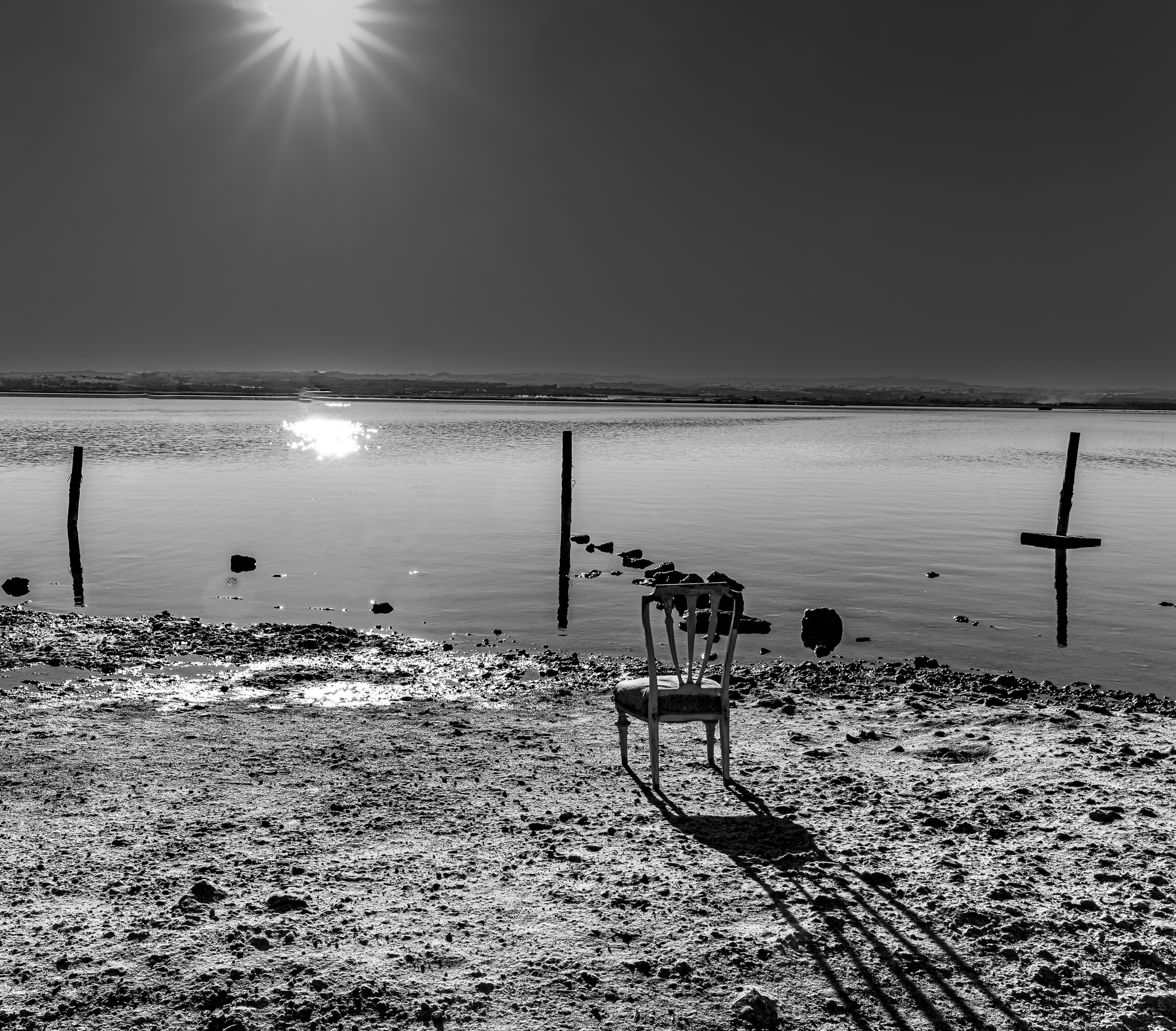 Silla abandonada con tres postes y starburst solar sobre el agua