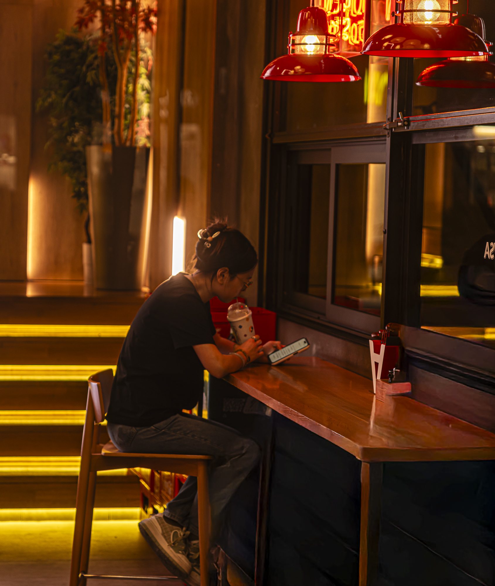 Chica sola con el móvil bajo lámparas rojas, escaleras iluminadas de ámbar