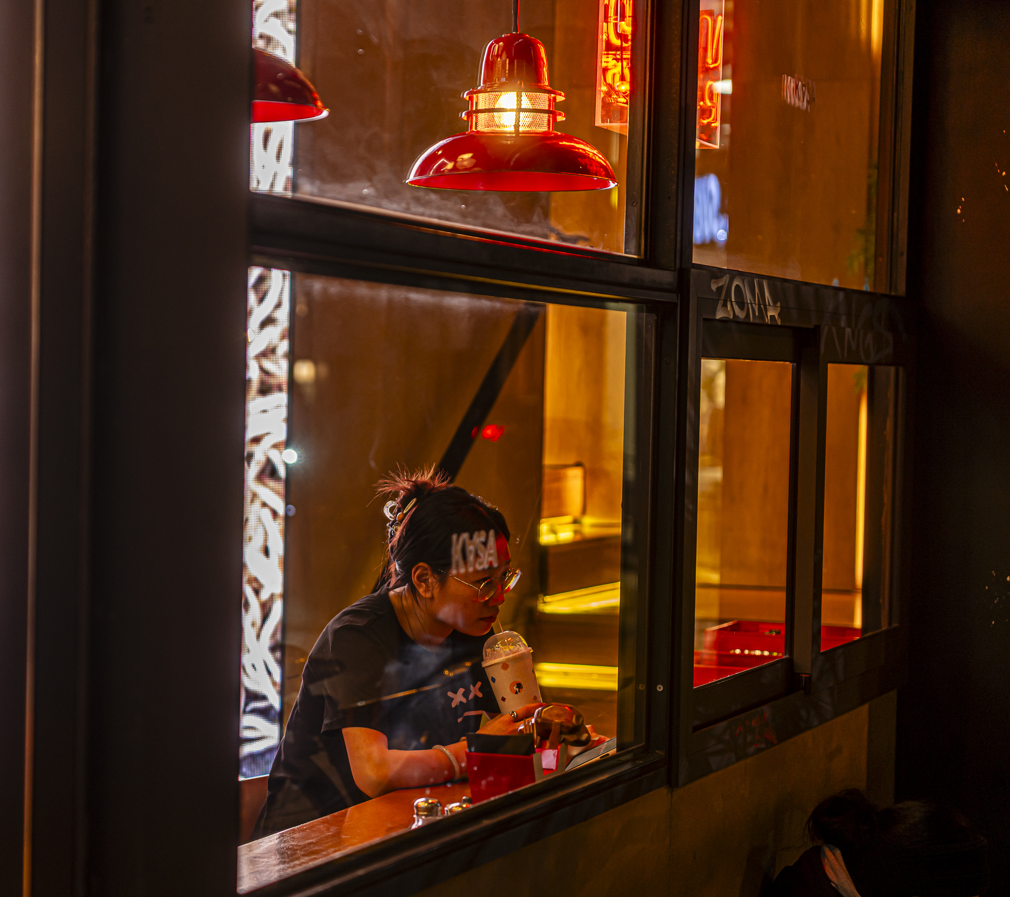 Chica con bubble tea observada a través del cristal, lámpara roja, reflejos