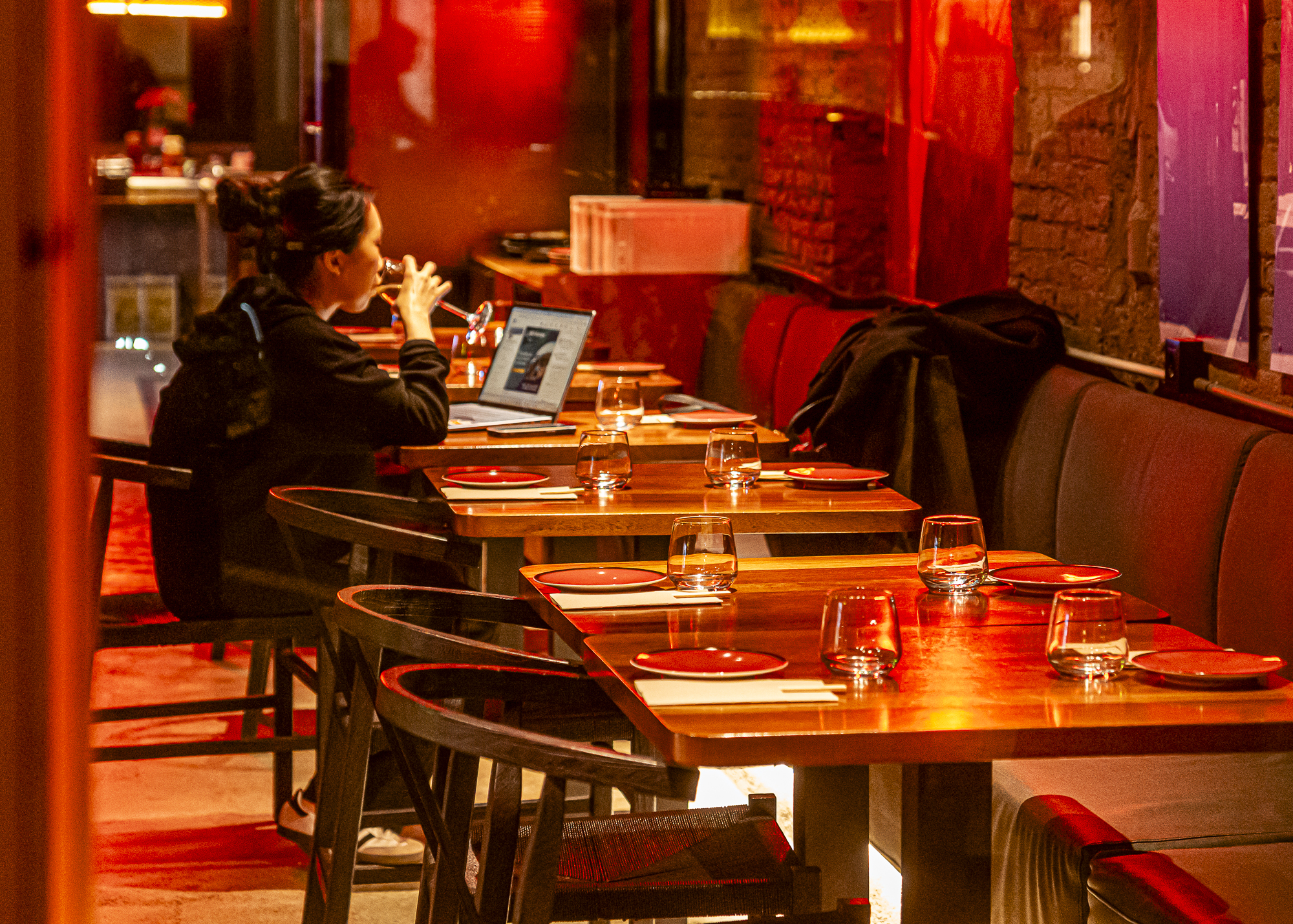 Mujer con laptop en restaurante vacío bañado en luz roja, copas y platos vacíos