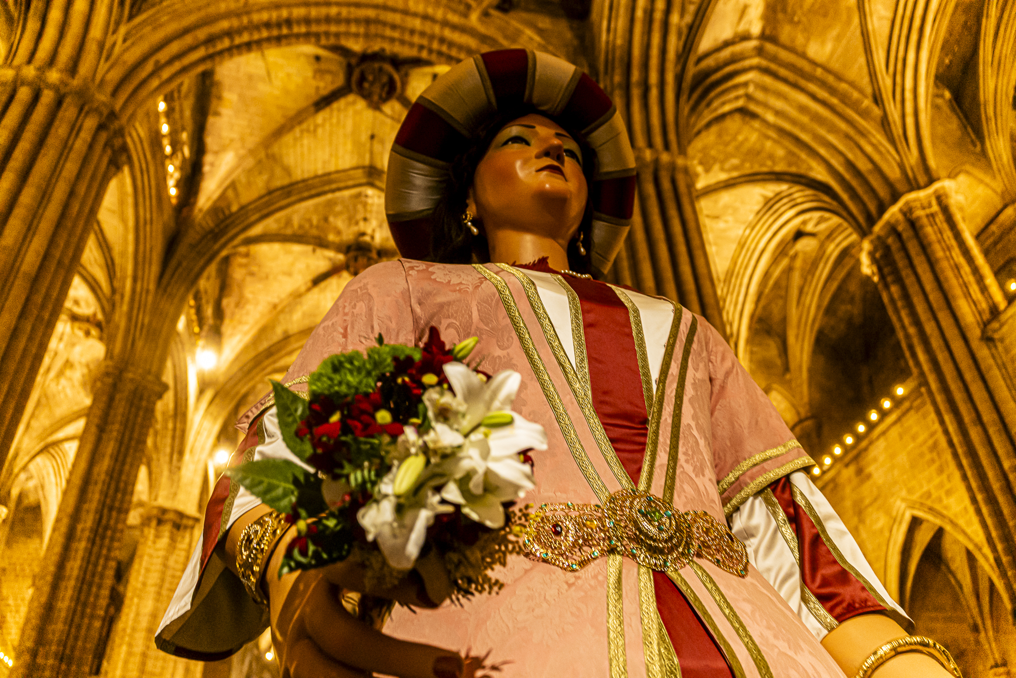 Elisenda mirando hacia las bóvedas góticas, nervaduras irradiando desde su cabeza