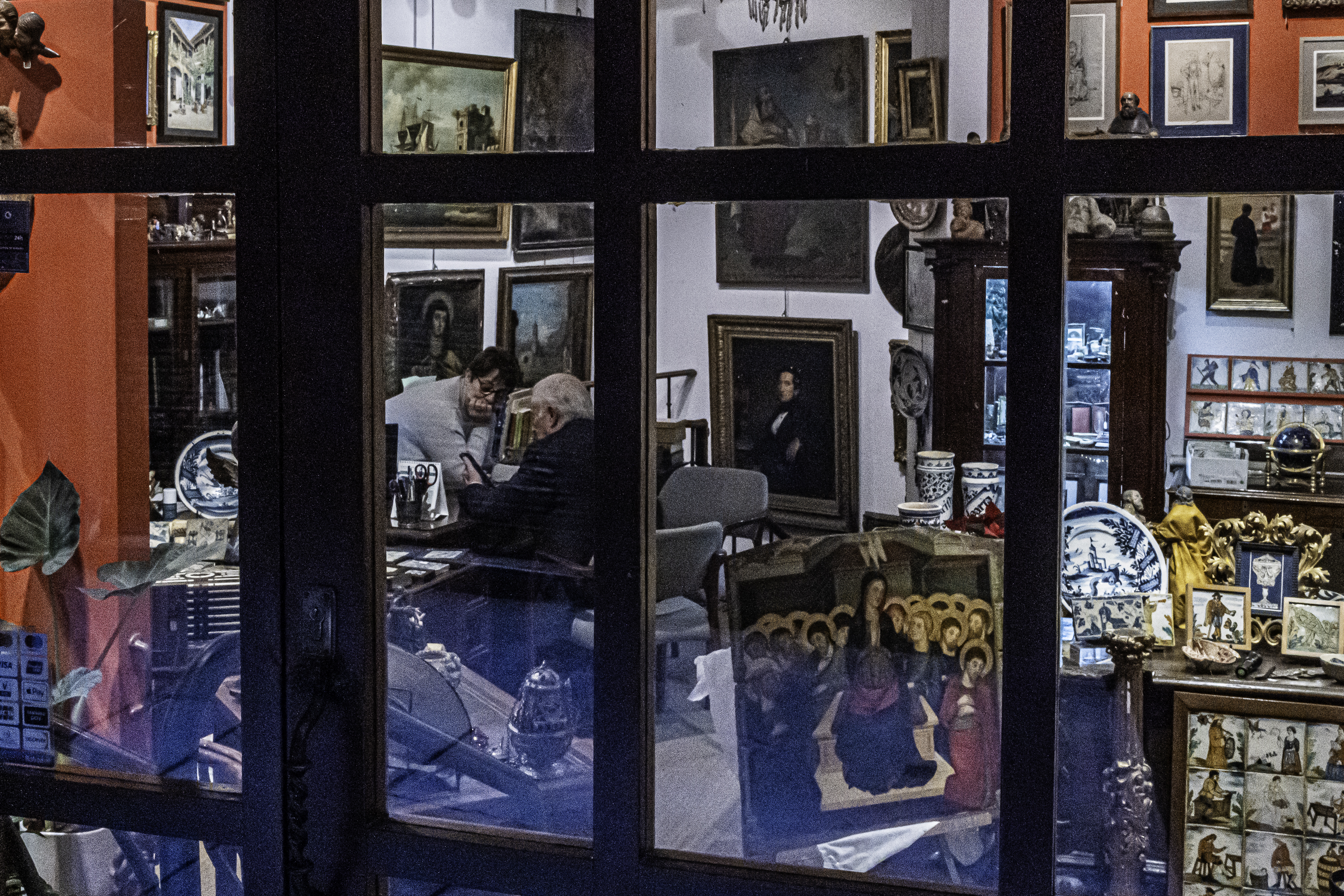 Anticuario trabajando entre cuadros y porcelana tras el escaparate