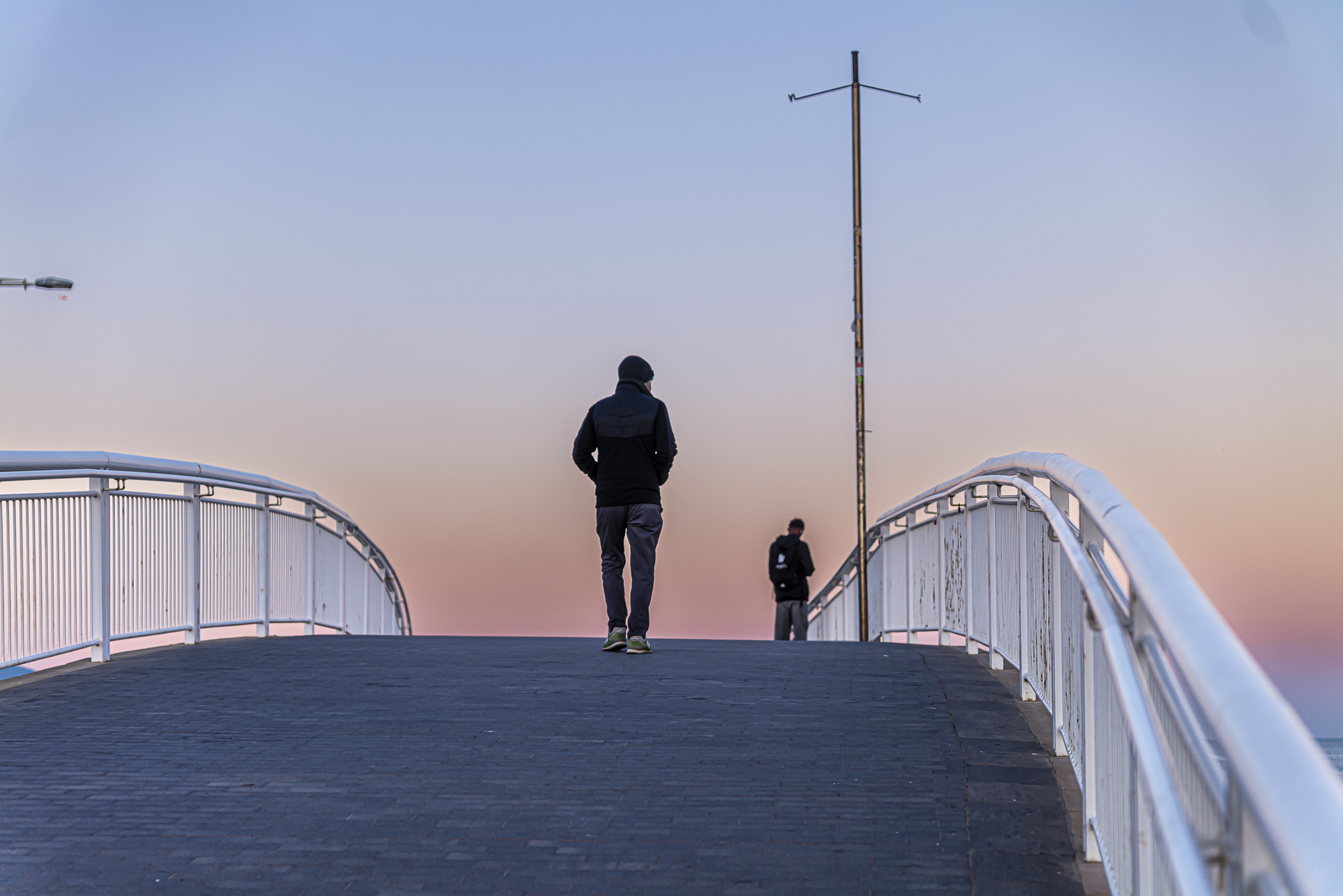 Hombre solo caminando de espaldas sobre el puente, cielo malva