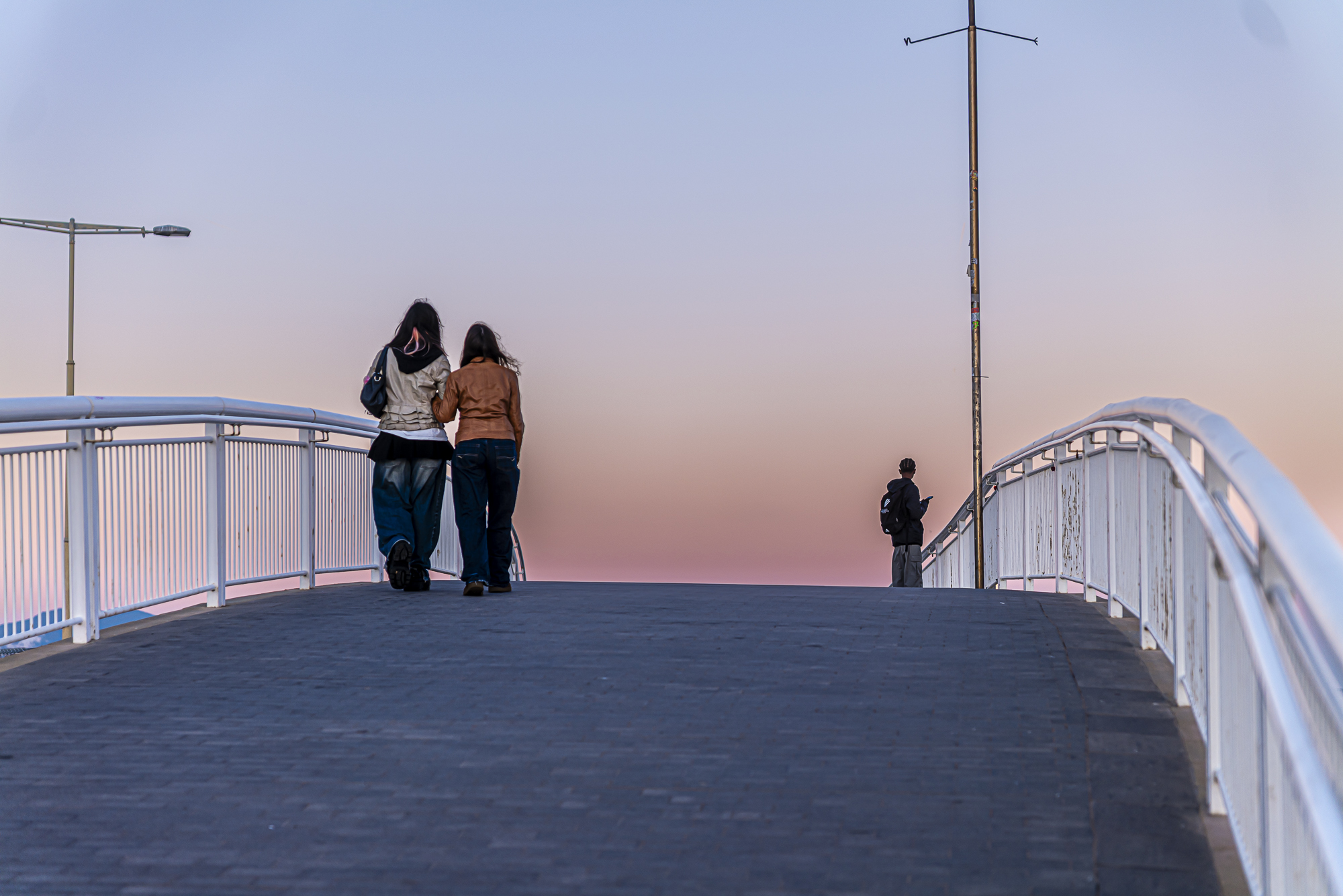 Pareja caminando juntas sobre el puente, cielo malva