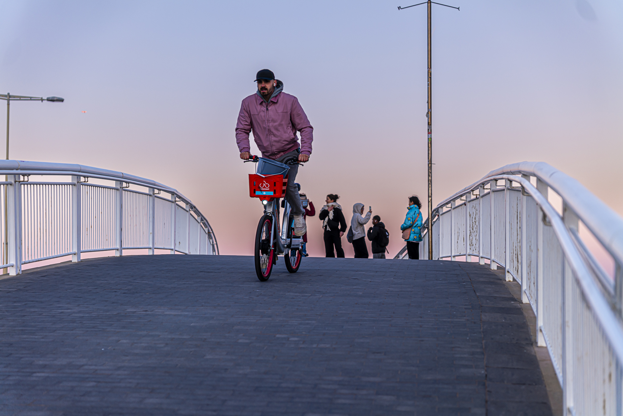 Ciclista con chaqueta rosa y bicicleta roja cruzando el puente de frente