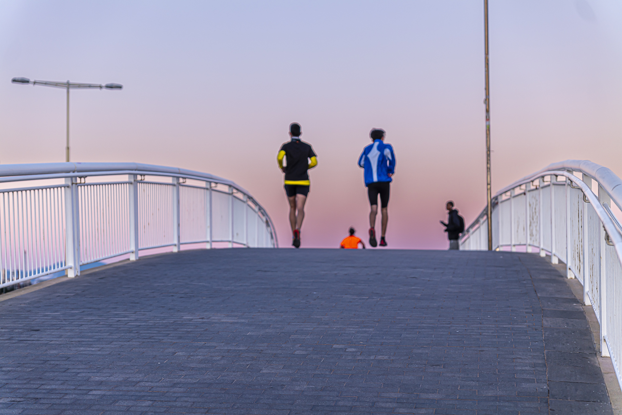 Dos corredores alejándose sobre el puente, niño con camiseta naranja sentado