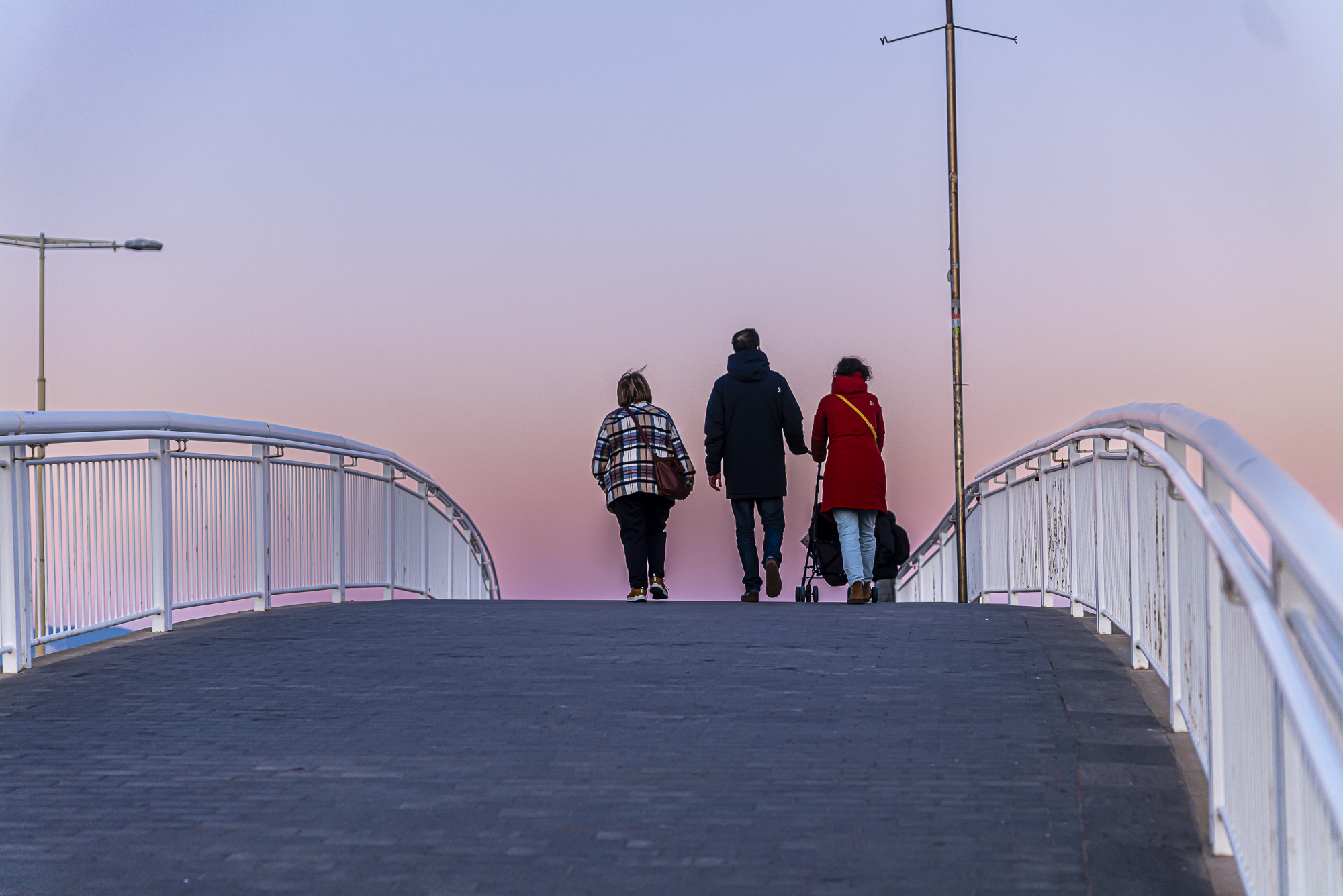 Familia caminando sobre el puente, abrigo rojo, carrito, cielo malva