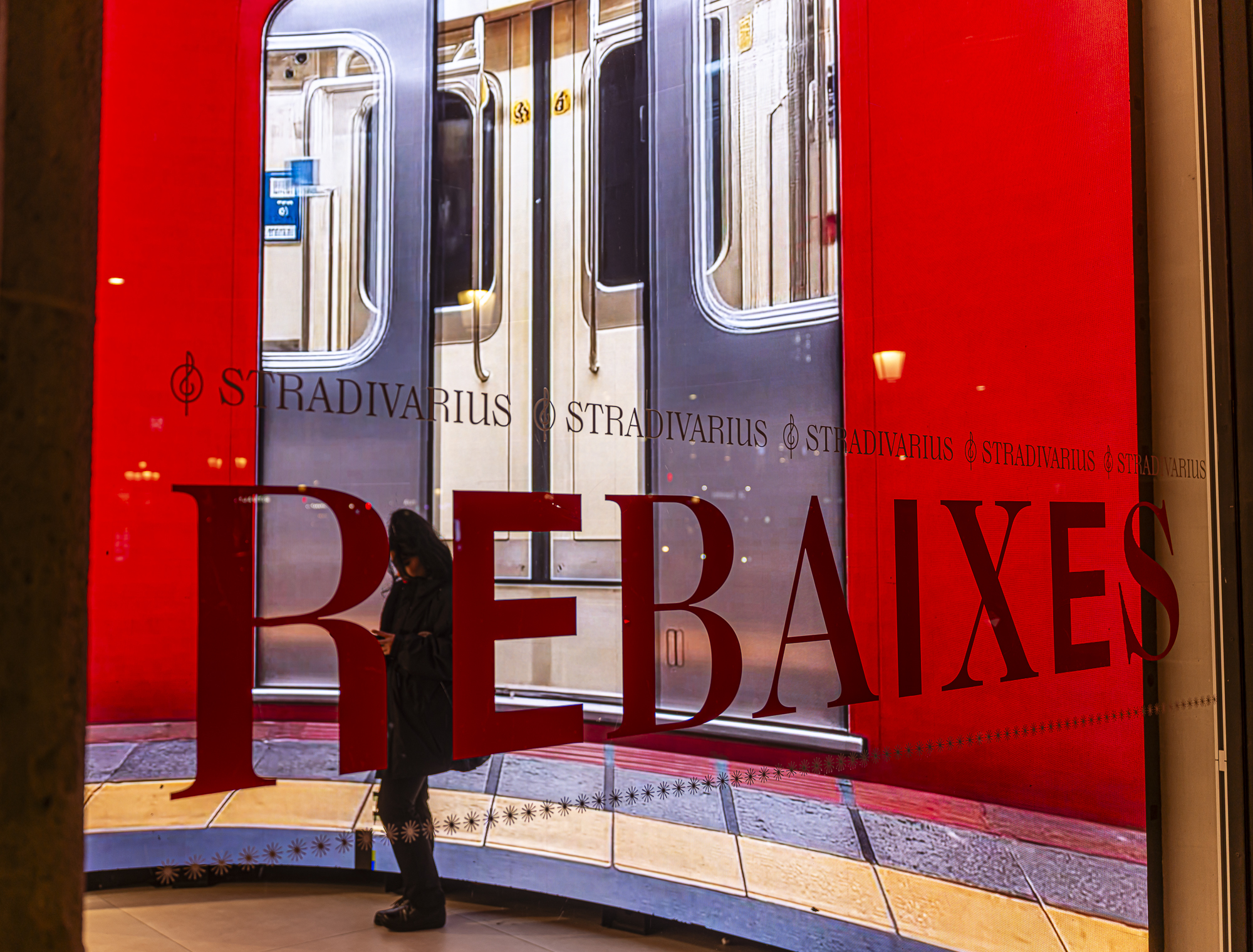 Silueta mirando el móvil ante el escaparate rojo de REBAIXES