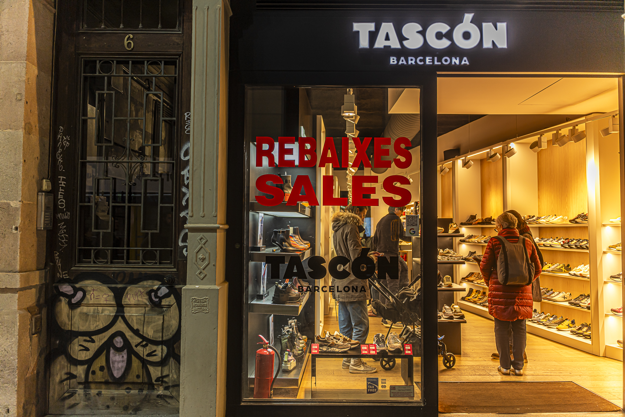 Puerta abandonada con graffiti junto a escaparate iluminado de zapatería