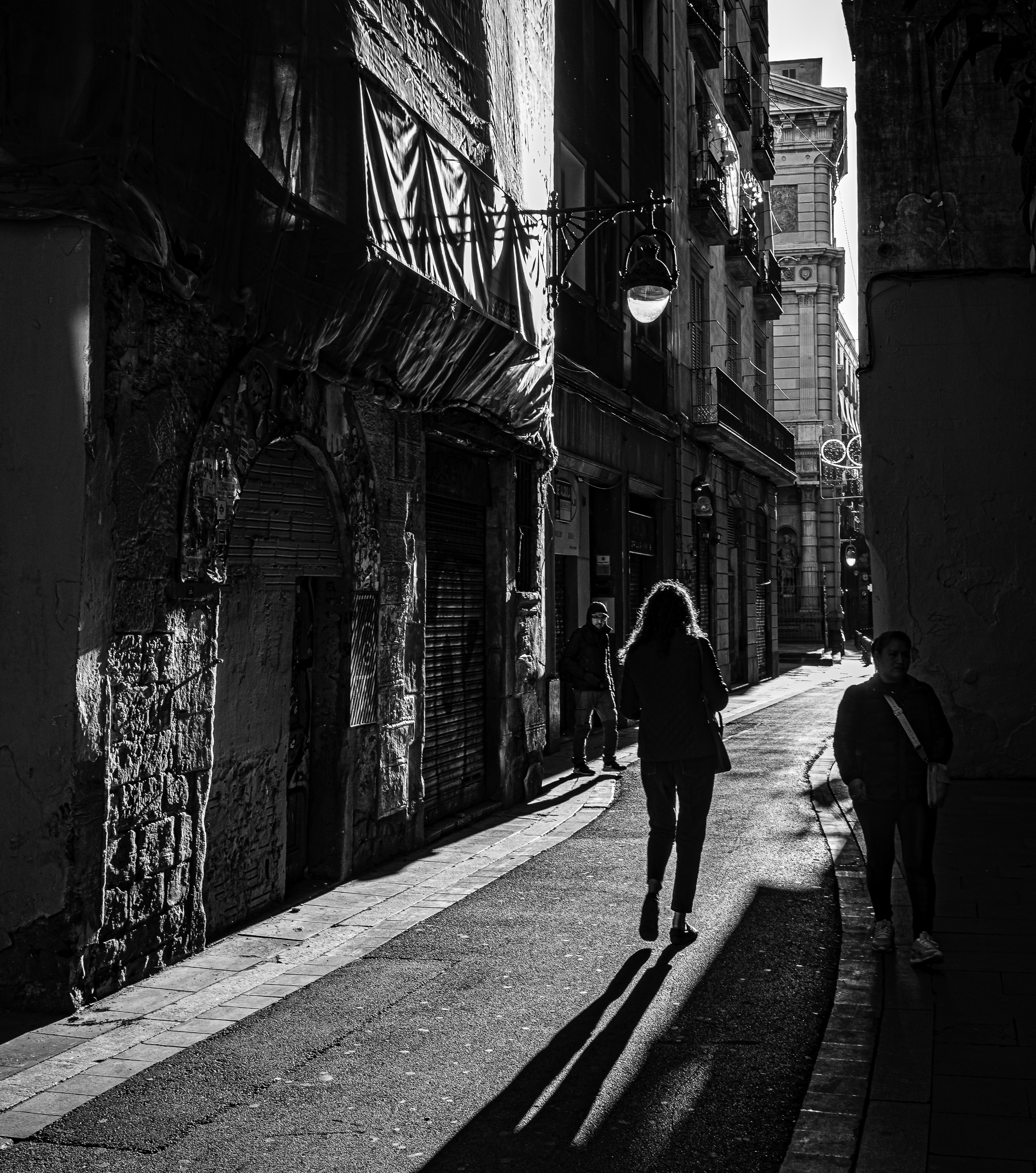 Silueta de mujer caminando por callejón del Gótico, sombra larga proyectada a contraluz