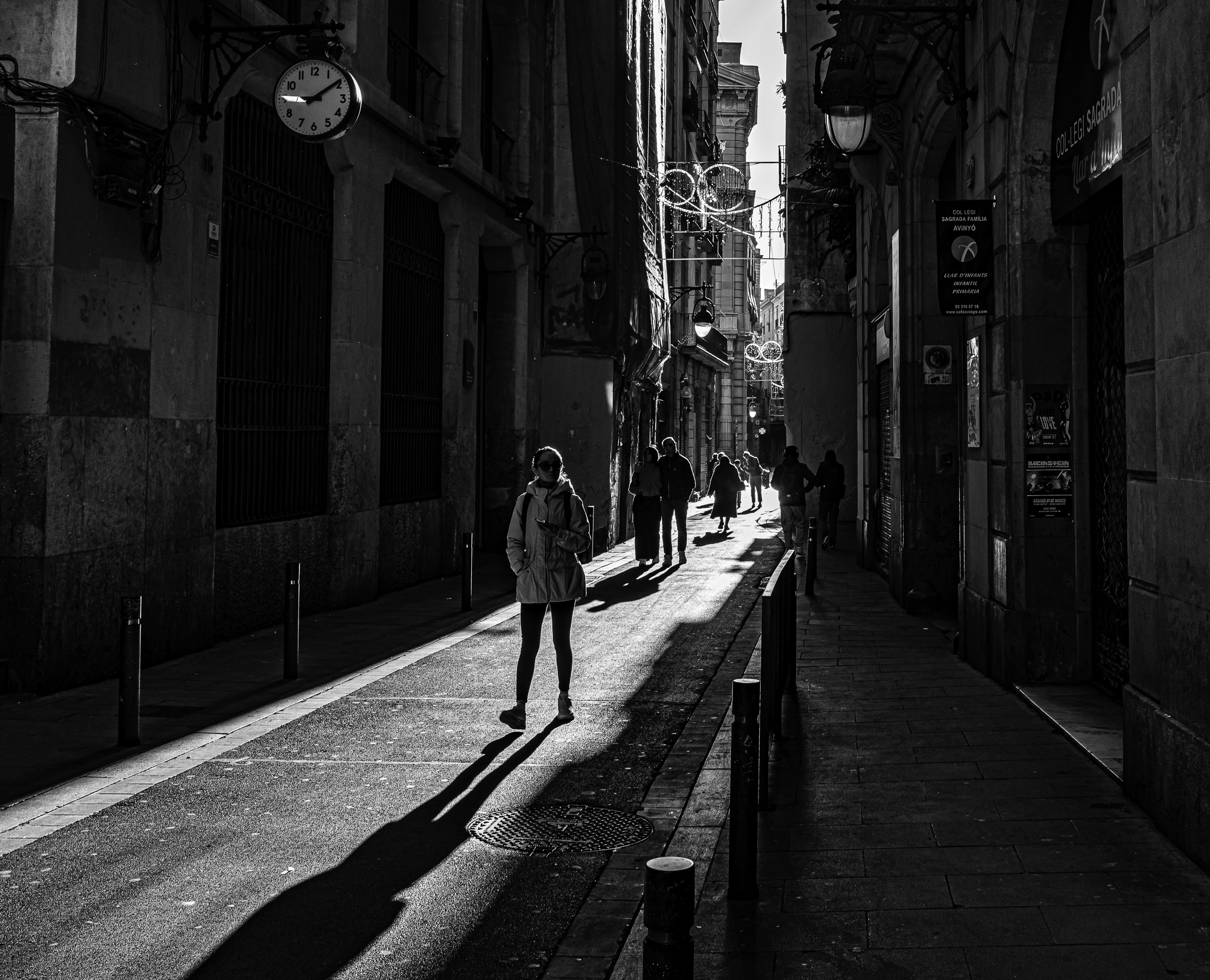 Mujer caminando bajo un reloj de pared, sombra alargada sobre el pavimento del Gótico