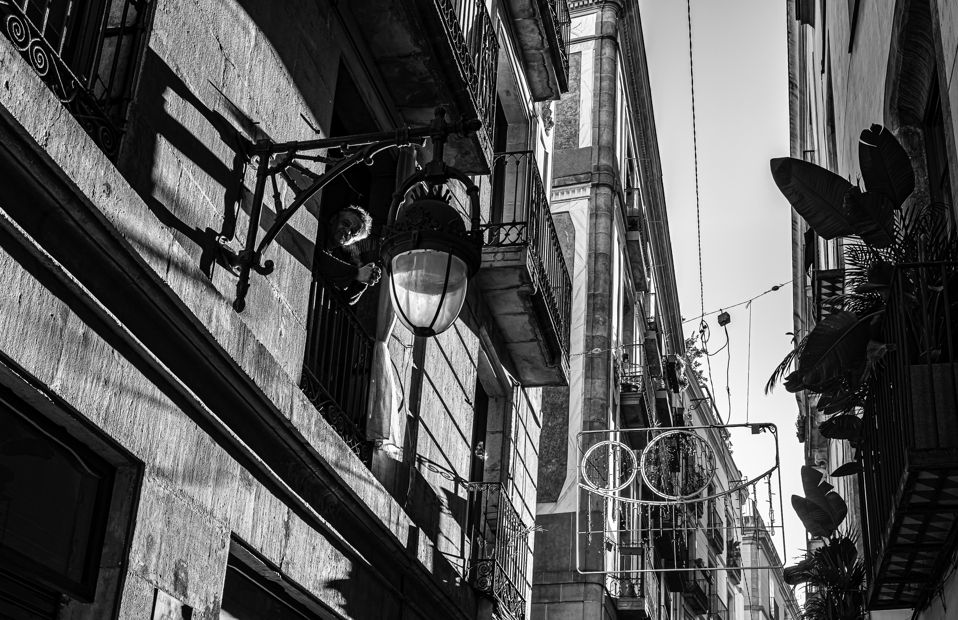Hombre asomado al balcón tras un farol de forja, sombras diagonales cruzando la fachada