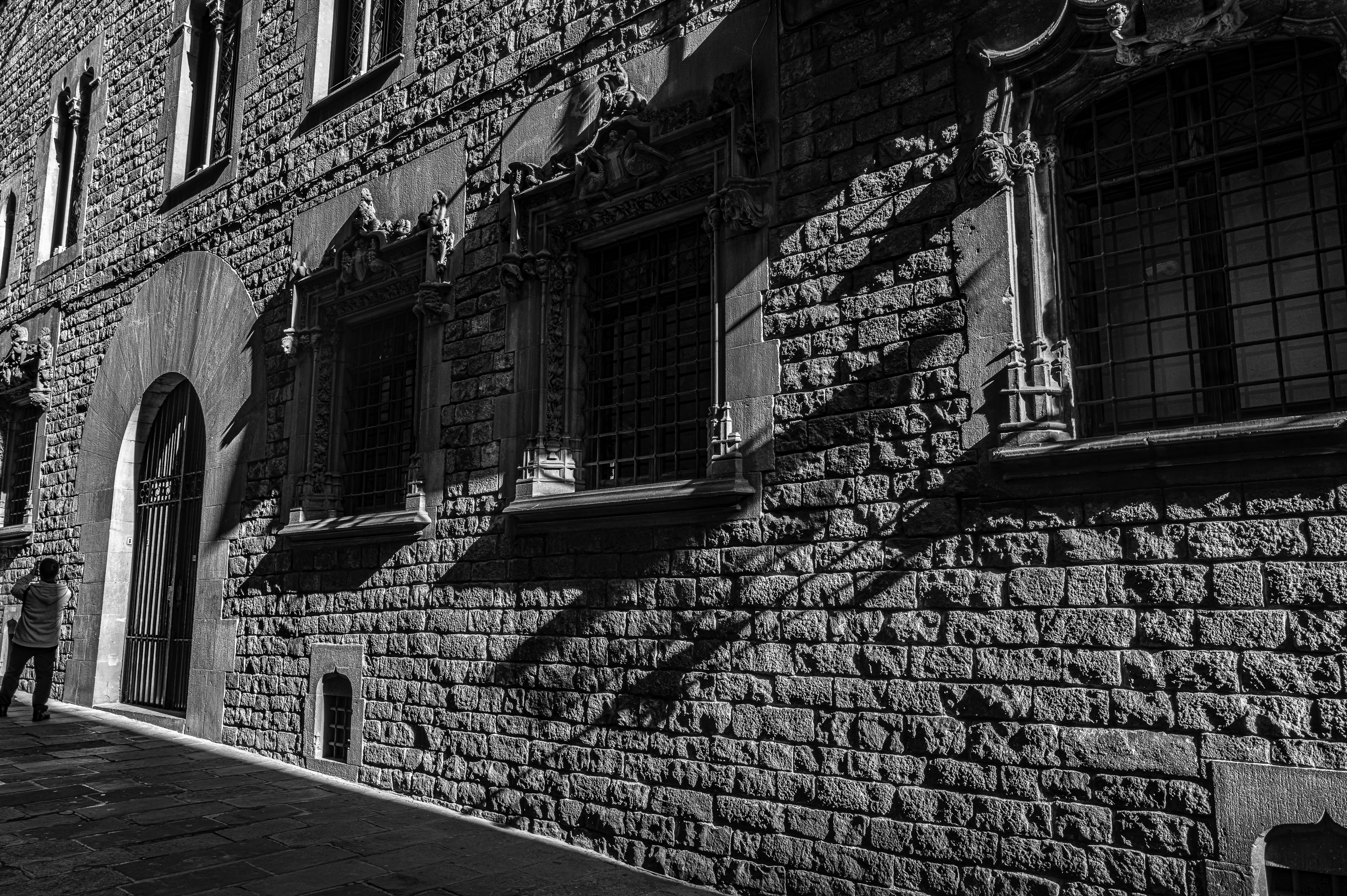 Fachada gótica de piedra con ventanas ornamentadas y sombras diagonales cruzándola