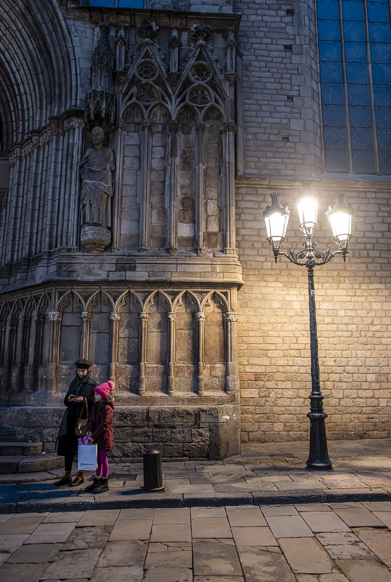 Madre inclinándose hacia su hija en los escalones, San Pedro observa desde su hornacina