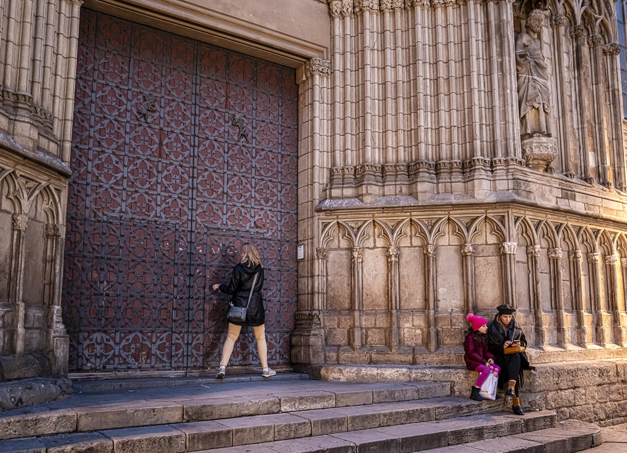 Chica empujando la puerta cerrada mientras madre e hija esperan sentadas en los escalones