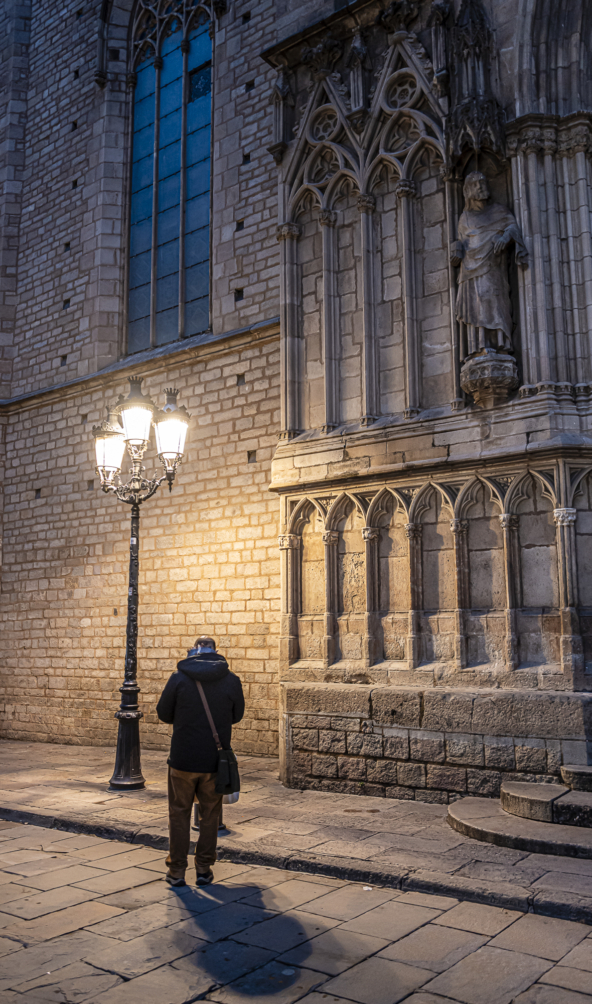 Figura solitaria caminando ante el muro de la basílica, farola encendida, San Pablo arriba