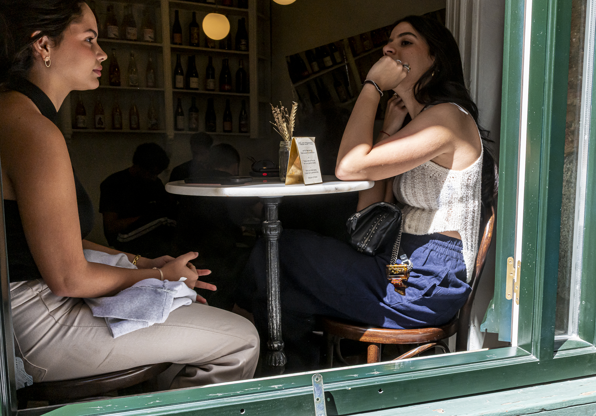 Dos chicas conversando en un café vistas a través del cristal verde