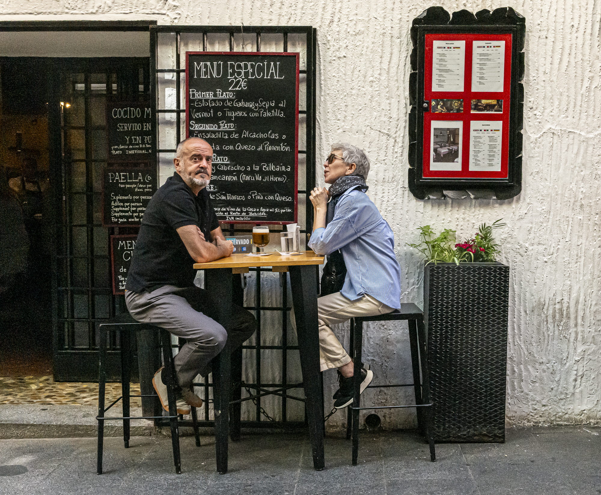 Pareja en terraza, ella habla, él mira directamente al fotógrafo