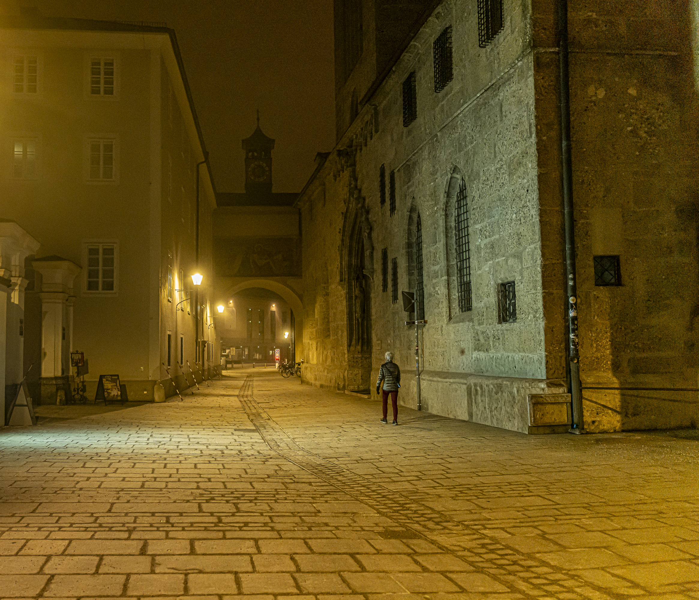 Solitary figure in medieval alley at night under golden fog